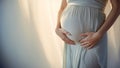 Pregnant woman wearing beautiful dress holding her hands on belly on a light background. Pregnancy, maternity, preparation and