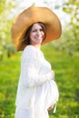 Pregnant woman wearing big hat and white dress in blooming garde Royalty Free Stock Photo