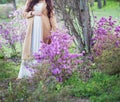 Pregnant woman in white dress and beige coat near blossom tree