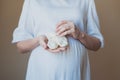 Pregnant woman in white dress holding baby socks with her hands near belly Royalty Free Stock Photo