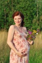 Pregnant woman with wild flowers touches belly at summ