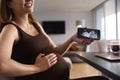 Pregnant Woman Working From Home On Laptop Looking At Phone With Ultrasound Scan Of Baby Royalty Free Stock Photo