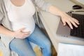 Pregnant woman working on laptop at her working place in office. Medical insurance childbearing. Maternity leave. Pregnancy and