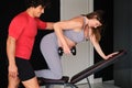 Pregnant woman working out with a dumbbell supervised by a personal trainer.