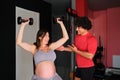 Pregnant woman working out with dumbbells with personal trainer at the gym. Royalty Free Stock Photo