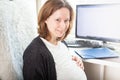 Pregnant woman works at home at a remote job, sits at a table with a computer