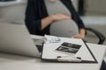 A pregnant woman works on a laptop in the office and looks at a photo from an ultrasound scan of the fetus. Belly close Royalty Free Stock Photo