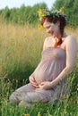 Pregnant woman in wreath sits and laughs in dry field Royalty Free Stock Photo