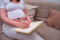 Pregnant woman writes in a notebook in the home interior, lifestyle