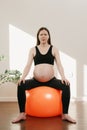 A pregnant woman is writhing in pain exhaling air with her arms on her knees