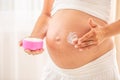 Pregnant woman& x27;s belly detail, one hand holding a moisturizer and the second applying the lotion on the skin Royalty Free Stock Photo