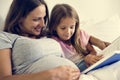 Pregnant woman and daugther reading book together on the bed Royalty Free Stock Photo