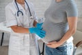 Pregnant woman visiting a doctor. Elderly caucasian female gynaecologist holds hands on the tummy of a pregnant patient. Royalty Free Stock Photo