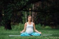 Pregnant yoga in the lotus position on the forest background. in the park the grass mat, outdoor, health woman. Royalty Free Stock Photo