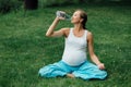 Pregnant yoga woman drinking water from a bottle, in the lotus position. park ,grass and ,.outdoor, forest. Royalty Free Stock Photo
