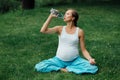 Pregnant yoga woman drinking water from a bottle, in the lotus position. park ,grass ,.outdoor, forest. Royalty Free Stock Photo