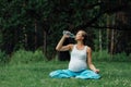 Pregnant yoga woman drinking water from a bottle, in the lotus position. park ,grass ,.outdoor, forest. Royalty Free Stock Photo