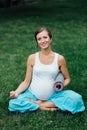 Pregnant yoga woman in the lotus position with mat portrait in park on the grass, breathing, stretching, statics. Royalty Free Stock Photo