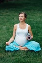 Pregnant yoga woman in the lotus position with mat portrait in park on the grass, breathing, stretching, statics. Royalty Free Stock Photo