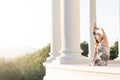 Pregnant yogi practicing in a building with columns watching the sunrise