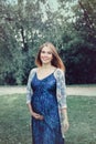 Pregnant young Caucasian woman wearing long blue dress posing in park Royalty Free Stock Photo