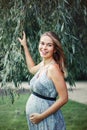 Pregnant young Caucasian woman wearing long blue dress and rustic country hat in park outside. Royalty Free Stock Photo