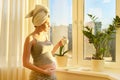 Pregnant young woman with bath towel on head with cup of tea looking out window Royalty Free Stock Photo