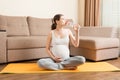 Pregnant young woman with bottle of water while sitting in lotus position on yoga mat. Maintaining water balance at coronavirus Royalty Free Stock Photo