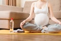 Pregnant young woman with bottle of water while sitting in lotus position on yoga mat. Maintaining water balance at coronavirus Royalty Free Stock Photo