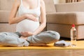 Pregnant young woman with bottle of water while sitting in lotus position on yoga mat. Maintaining water balance at coronavirus Royalty Free Stock Photo