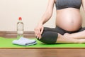 Pregnant young woman with bottle of water while sitting in lotus position on yoga mat. Maintaining water balance at coronavirus Royalty Free Stock Photo