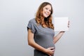 Pregnant young woman holding a blank canvas in her hands. Pregnancy concept, expecting a baby.