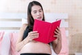 Pregnant young woman sitting with pillow on the bed while reading knowledge book in her hands at home. Pregnancy relax Royalty Free Stock Photo