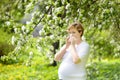Pregnant young woman sneezing and wipes nose with napkin during walking in spring park. Flu season, cold rhinitis. Allergic people Royalty Free Stock Photo