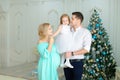 Pregnant young woman standing near husband keeping little daughter near Christmas tree.