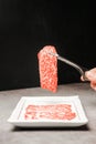 Premium Rare Slices sirloin Wagyu A5 beef with high-marbling texture on a ceramic plate, pick up by bbq tongs.