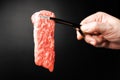 Premium Rare Slices sirloin Wagyu A5 beef with high-marbling texture pick up by bbq tongs with hand on black background. Served Royalty Free Stock Photo