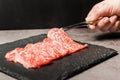 Premium Rare Slices sirloin Wagyu A5 beef with high-marbling texture pick up by bbq tongs with hand from stone plate. Served for