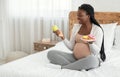 Prenatal Nutrition. Black Pregnant Woman Choosing Between Apple And Donuts At Home Royalty Free Stock Photo