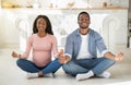 Prenatal yoga concept. Black pregnant woman and her husband meditating together on floor at home, panorama Royalty Free Stock Photo