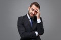 Preoccupied tired young bearded business man in classic black suit shirt tie posing isolated on grey background