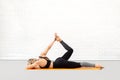 Prep bow pose, one side extension. Caucasian attactive woman in black sportswear lying on the mat and does body