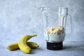 Preparation of a banana cocktail. Glass blender with banana slices and milk on a bluish gray background. Next to the blender are t