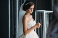 Preparation of the bride on a wedding day. Beautiful brunette girl in a white luxury dress, with earrings, make-up and Royalty Free Stock Photo