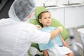 Preparation before the dentist check up. A seven-year-old girl sits in a dental chair, nurse adjusts her napkin.