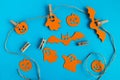 Preparation for Halloween. Orange paper decorations - ghosts, pumpkins and bats on a rope with pins on a blue background.