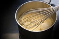 Preparation of hollandaise sauce, egg mixture is whisked at low temperature until foamy in a steel pot on a black cooktop, cooking