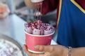 The preparation of ice-cream , Thai street food. cook pours purple ice cream in a paper Cup with cherry syrup