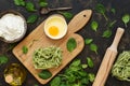 Preparation of pasta with spinach. Raw pasta on a cutting board, flour, eggs, spinach leaves on a capacious background. Top view.