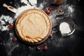 Preparation for pizza, flour and tomatoes on a round wooden board on a black wooden table